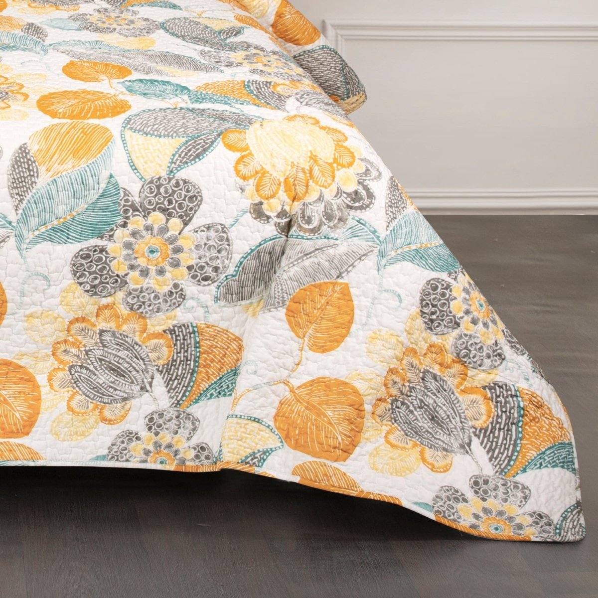 Floral patterned quilt with orange, yellow, and gray colors on a bed.