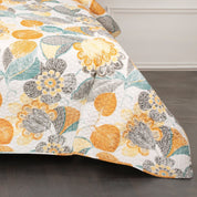 Floral patterned quilt with orange, yellow, and gray colors on a bed.