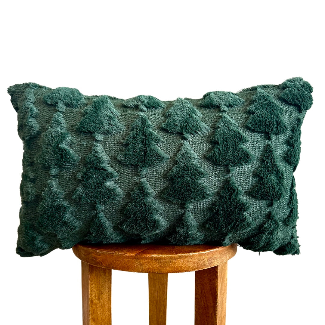 A dark green textured throw pillow with a raised tree pattern, displayed on a wooden stool against a white background.