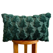 A dark green textured throw pillow with a raised tree pattern, displayed on a wooden stool against a white background.