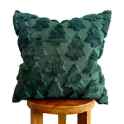 A dark green textured throw pillow with a raised tree pattern, displayed on a wooden stool against a white background.