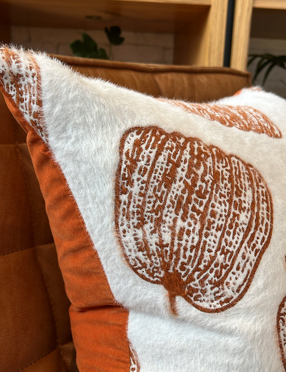 Close-up of a decorative pillow with brown leaf pattern on a wooden shelf background