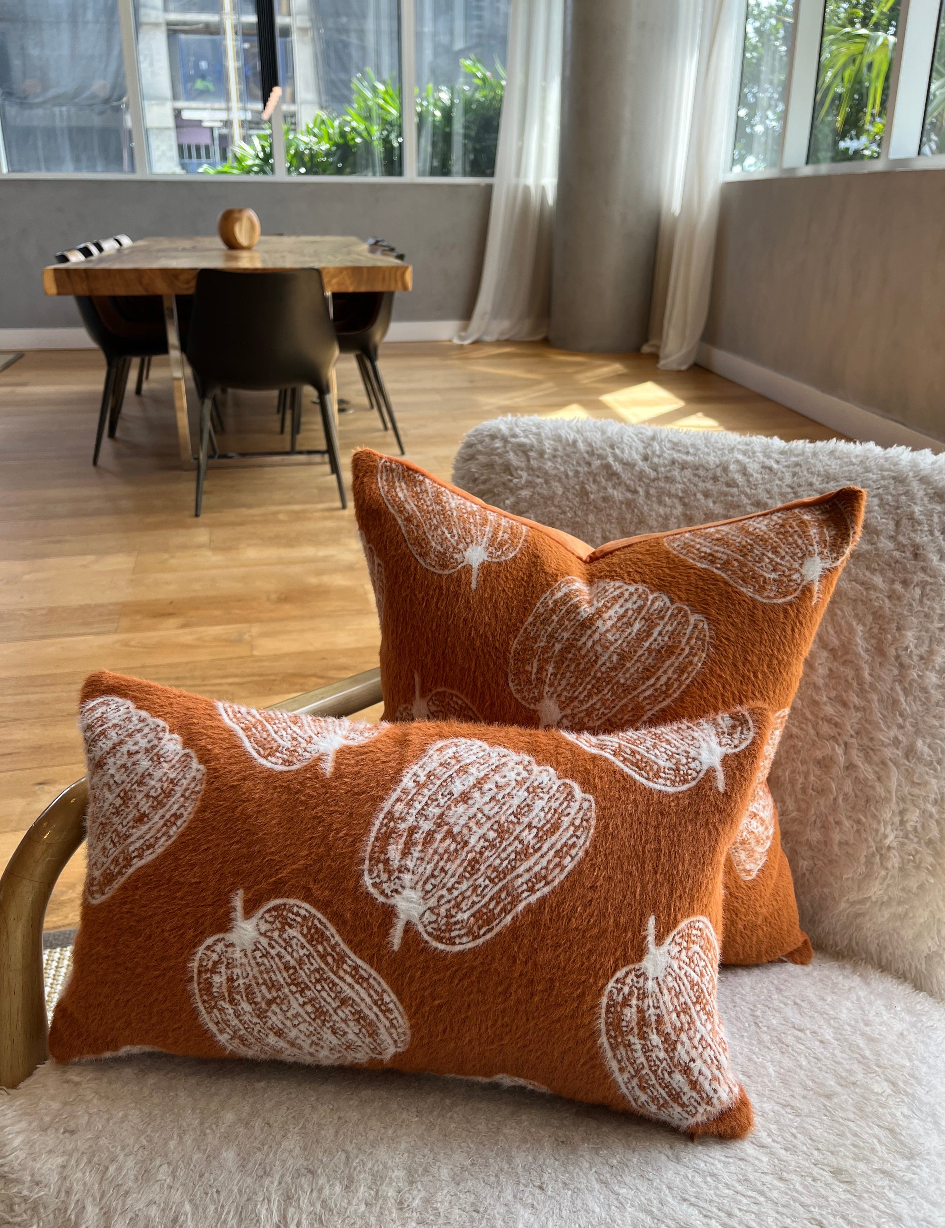 Orange pillows with white patterns on a sofa in a living room with a dining area in the background.