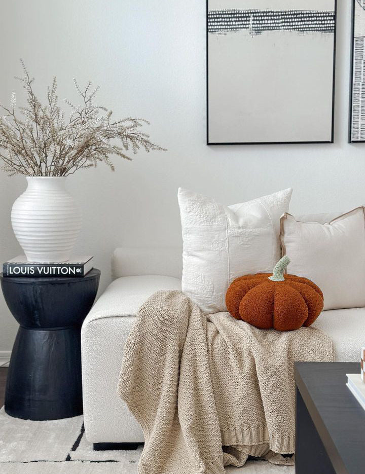Living room with a white sofa, beige blanket, and orange pumpkin decoration.