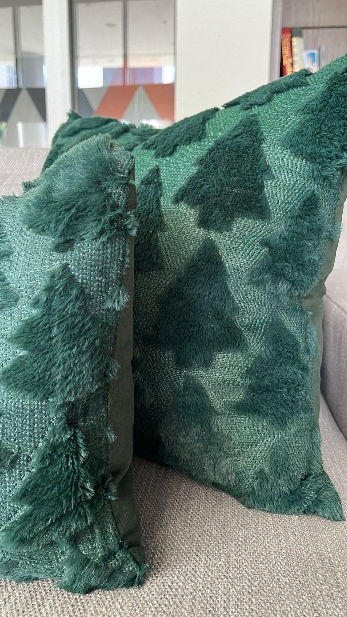 Two green textured throw pillows with a tree pattern and shaggy fringe, resting on a light beige sofa in a modern living room setting.