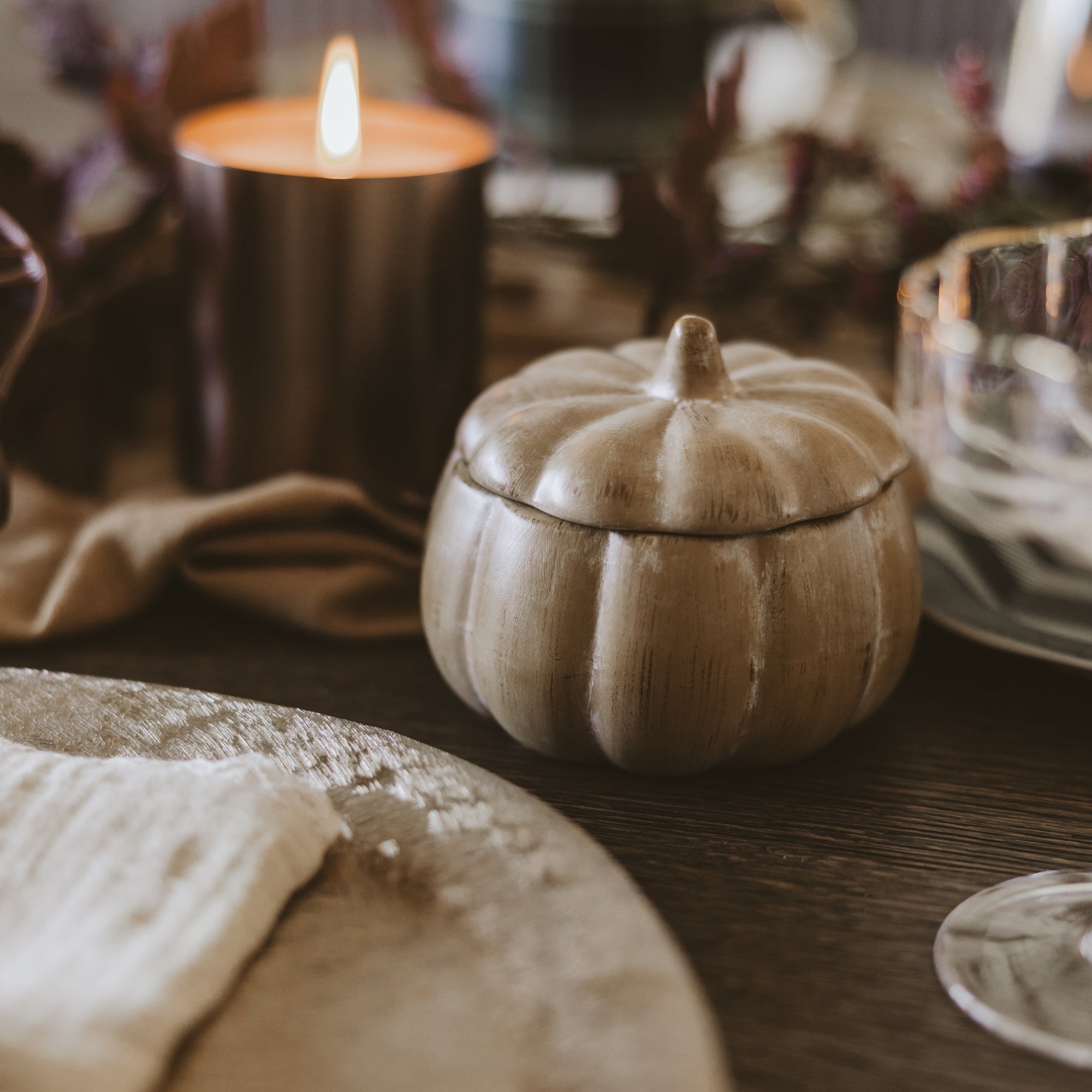 Decorative pumpkin-shaped container on a wooden surface with candles in the background