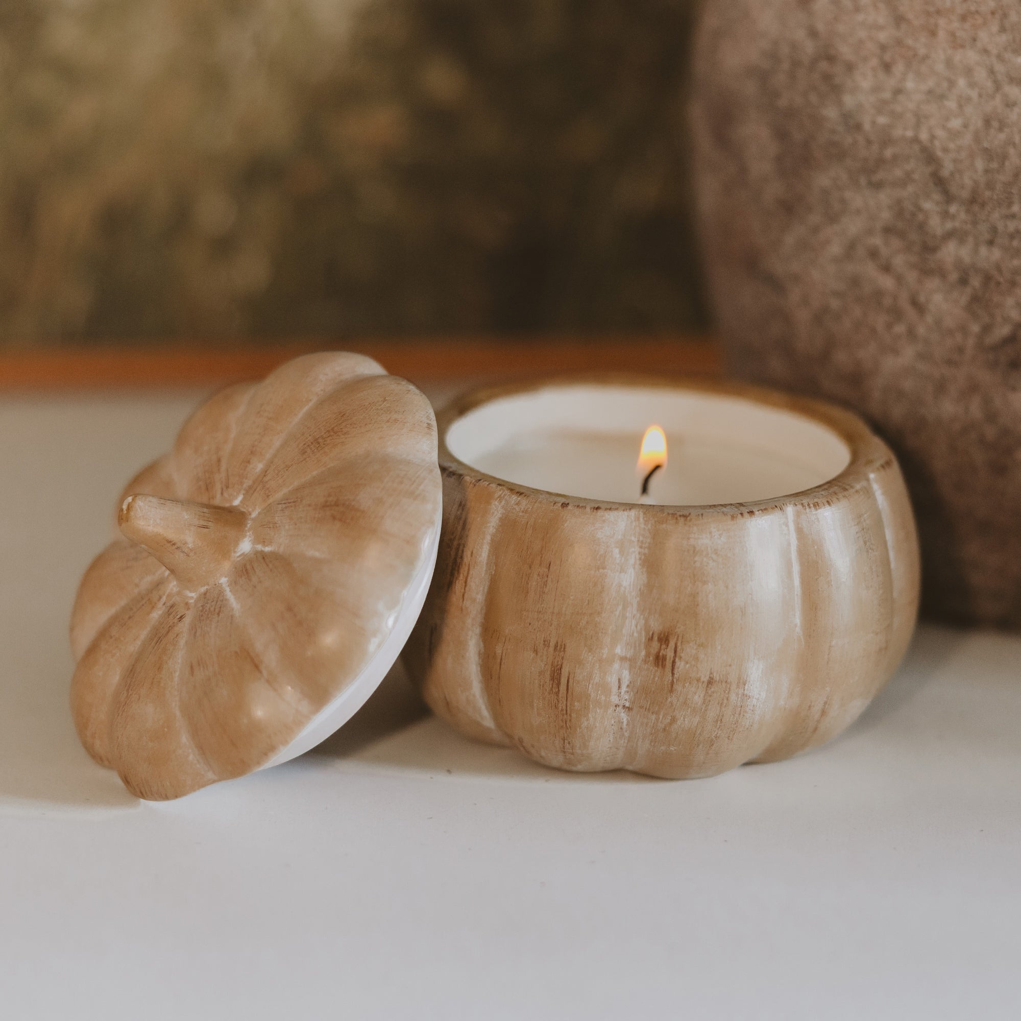 Wooden pumpkin-shaped candle holder with a lit candle on a neutral background