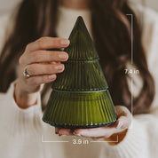 A person holds a small ribbed glass Christmas tree-shaped container in olive green. White measurement lines and text indicate dimensions of 7.