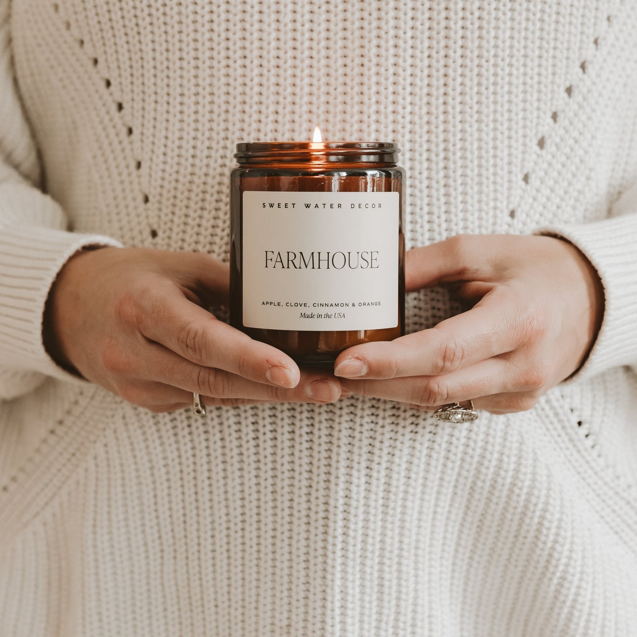 Person holding a 'Farmhouse' candle in a textured sweater