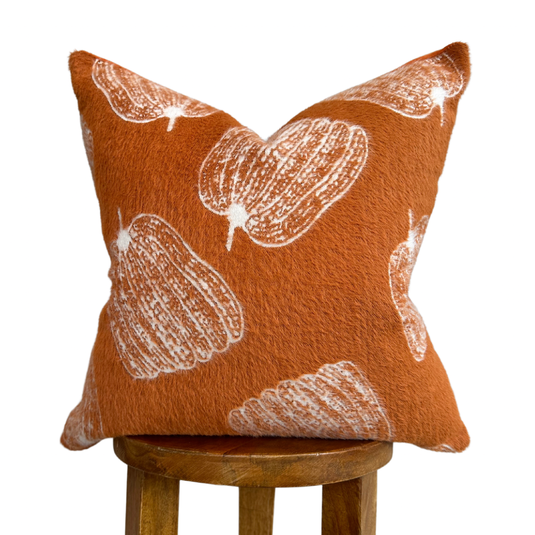 Orange pillow with white floral patterns on a wooden stool against a white background