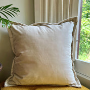 Beige pillow on a couch next to a window with greenery outside