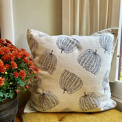 Decorative pillow with pumpkin pattern on a chair next to a potted plant.