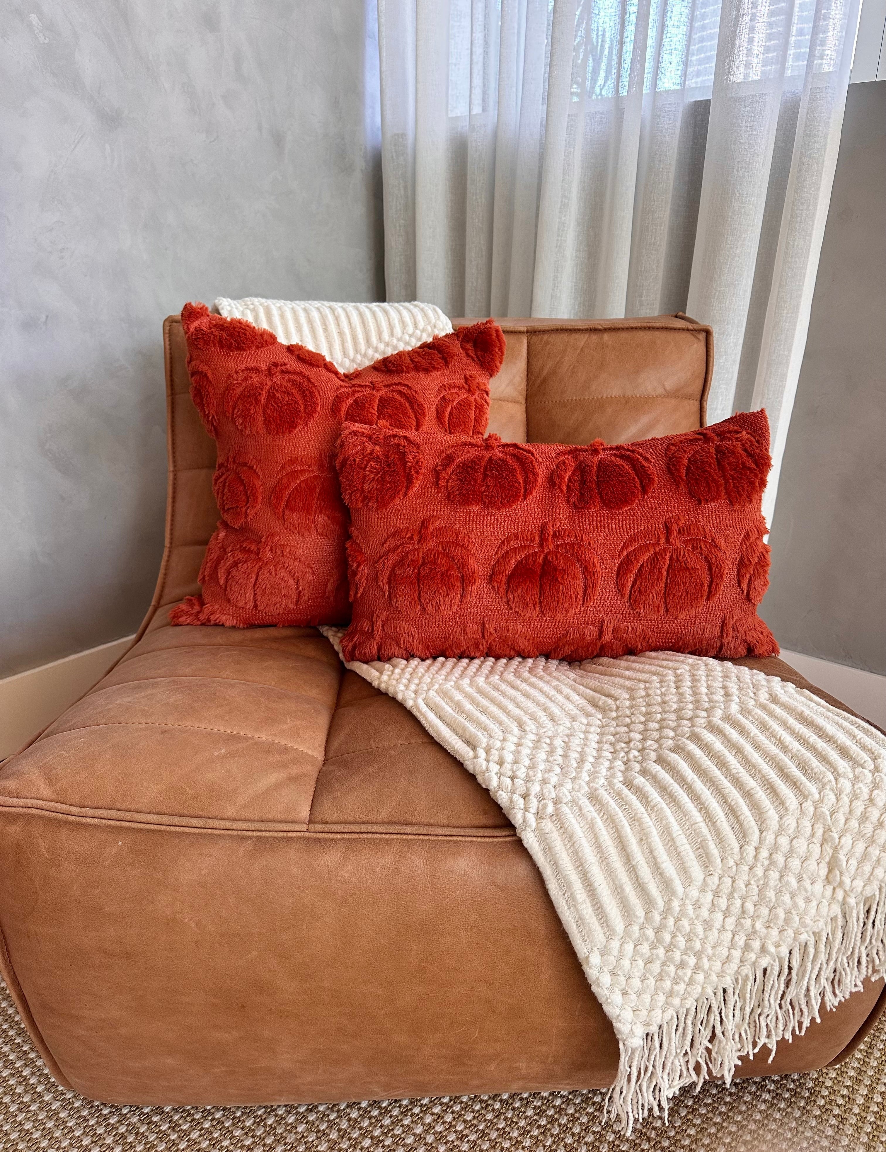 Brown leather chair with red textured pillows and a white blanket