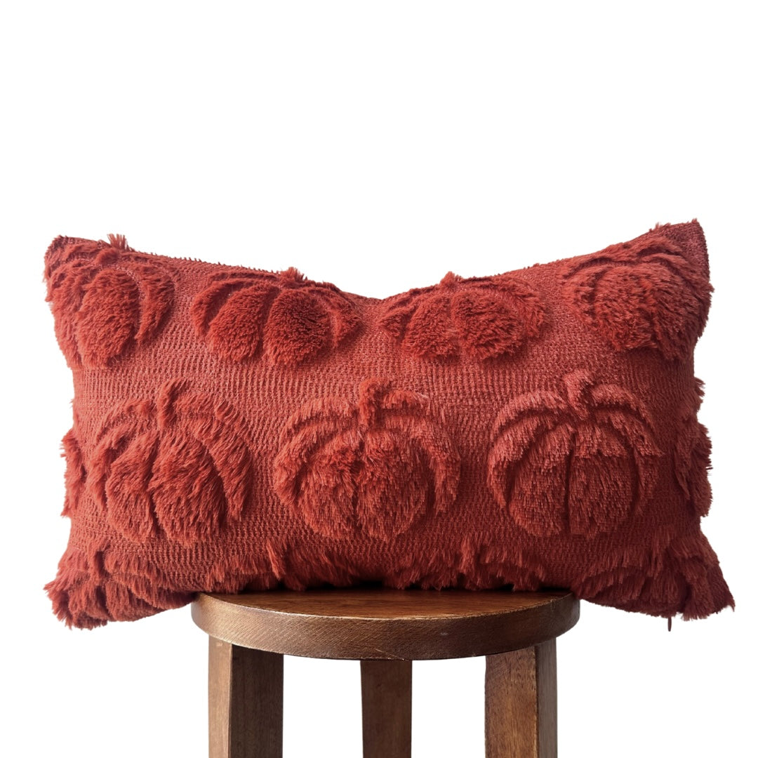 Red textured pillow with pumpkin pattern on a wooden stool against a white background