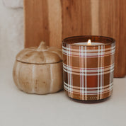 Candle with plaid design next to a pumpkin on a neutral background