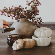 Decorative setting with a vase of flowers, candles, and pumpkin-shaped containers on a wooden surface.