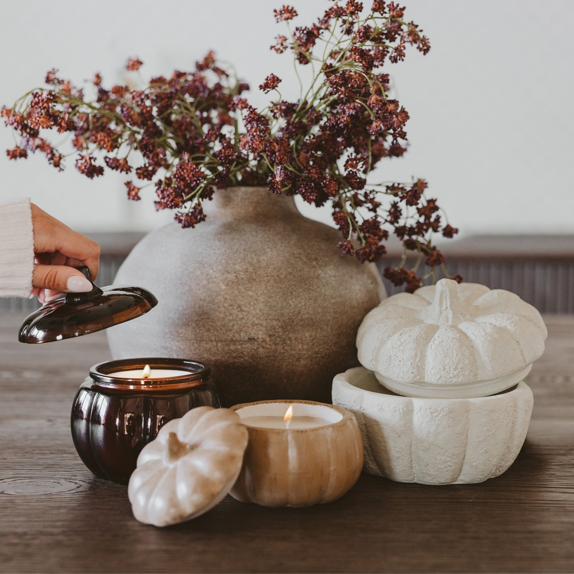 Decorative setting with a vase of flowers, candles, and pumpkin-shaped containers on a wooden surface.