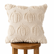 A square cream throw pillow with a raised, textured pumpkin pattern, resting on a wooden stool against a solid white background.