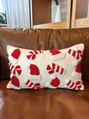 A rectangular throw pillow with a red and white candy cane and Santa hat pattern, resting on a brown leather sofa.