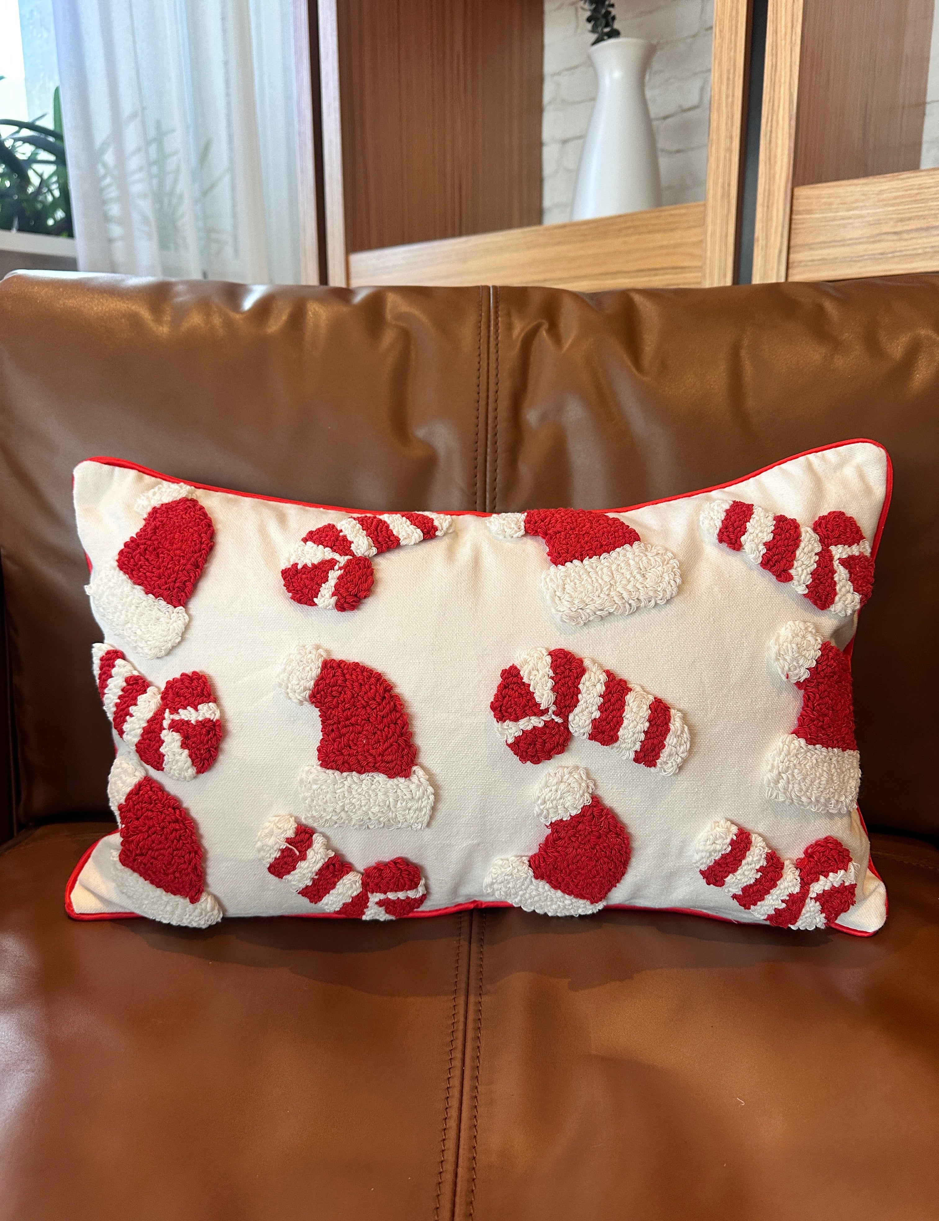 A rectangular throw pillow with a red and white candy cane and Santa hat pattern, resting on a brown leather sofa.