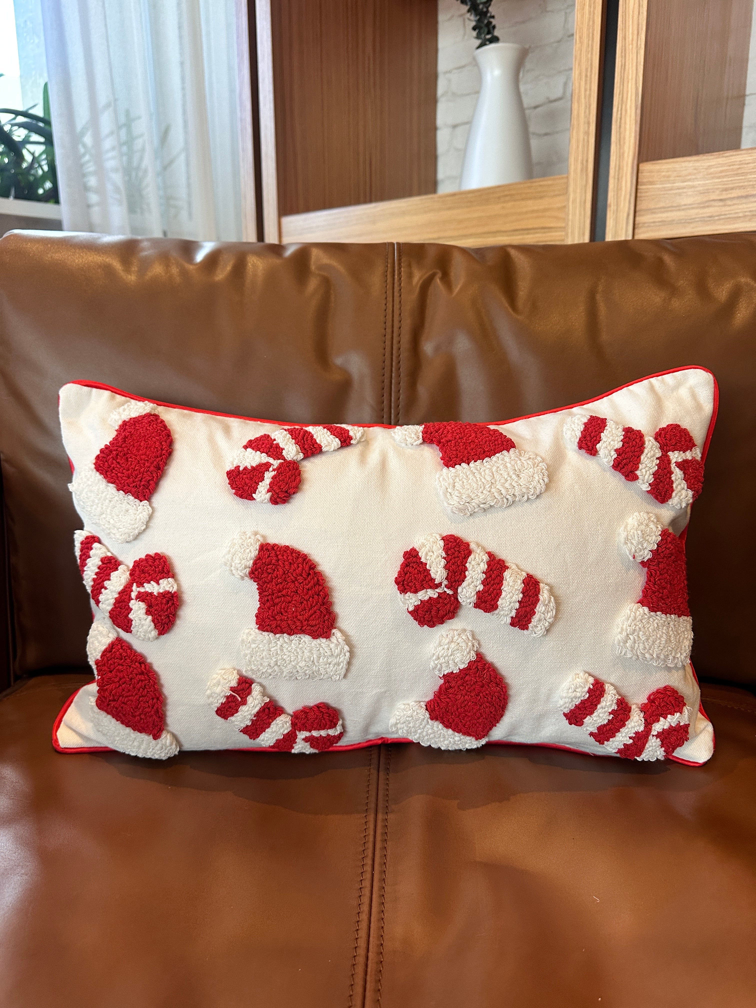 A rectangular throw pillow with a red and white candy cane and Santa hat pattern, resting on a brown leather sofa.
