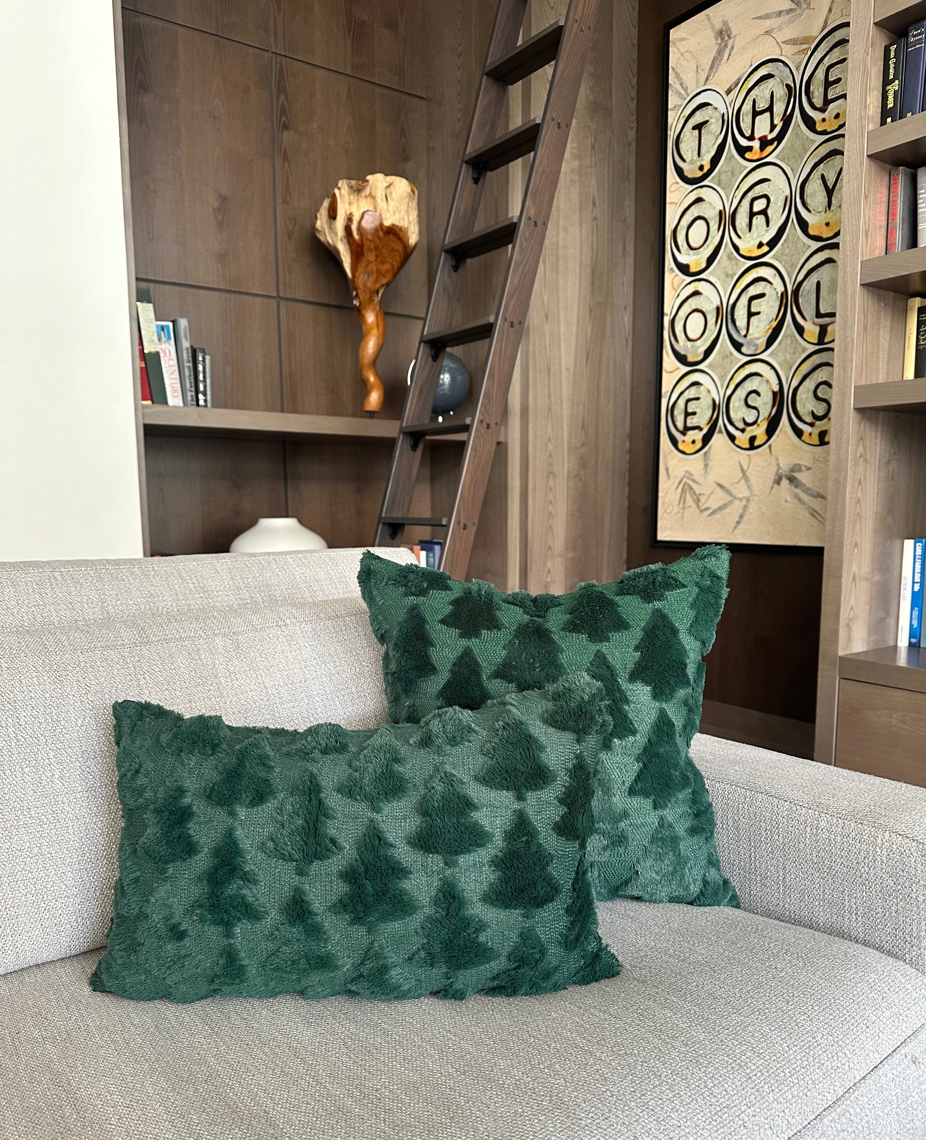 Two dark green textured throw pillows with a pine tree pattern resting on a light beige sofa in a cozy, modern living room setting.