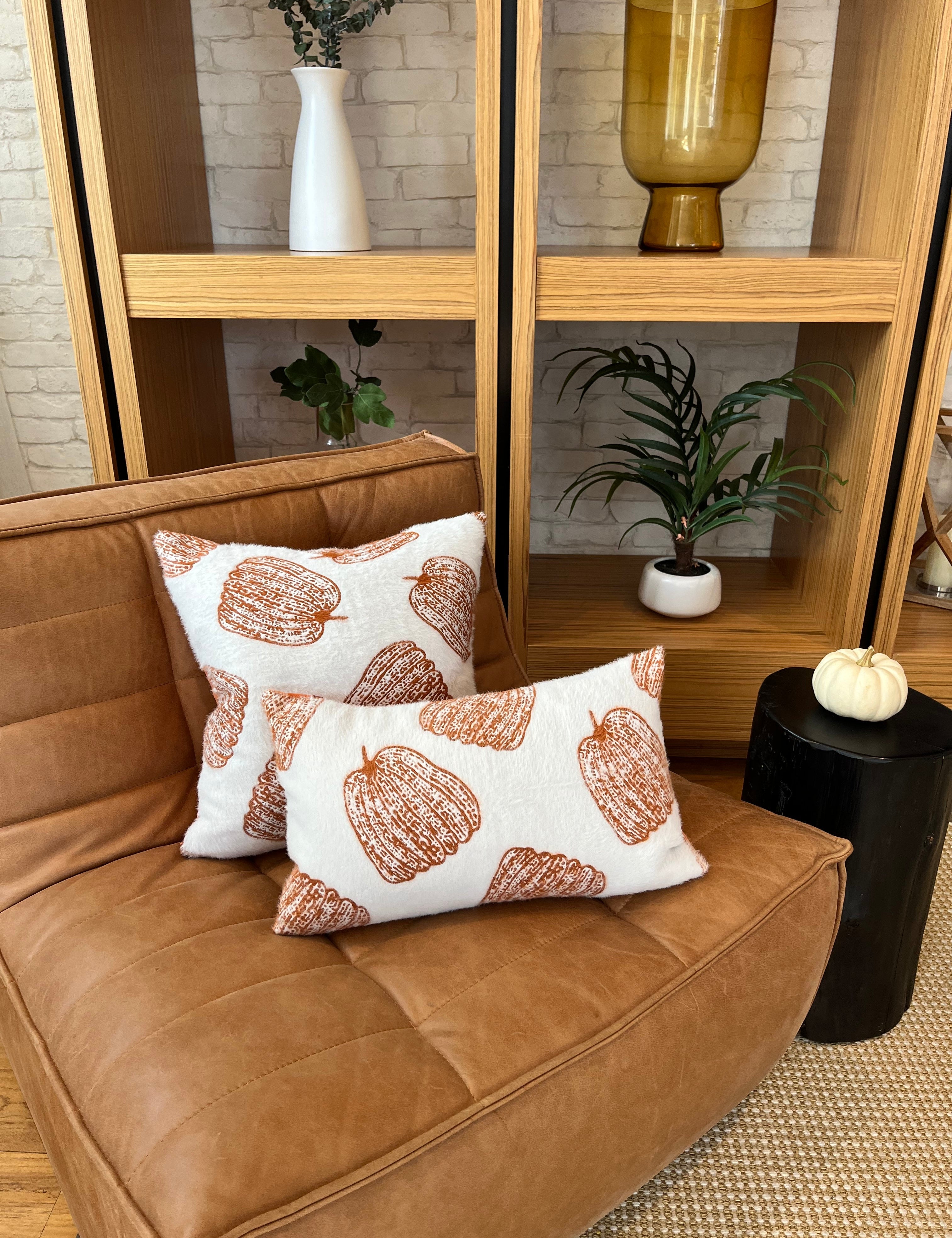 Brown leather sofa with decorative pillows in a room with wooden shelves and plants.