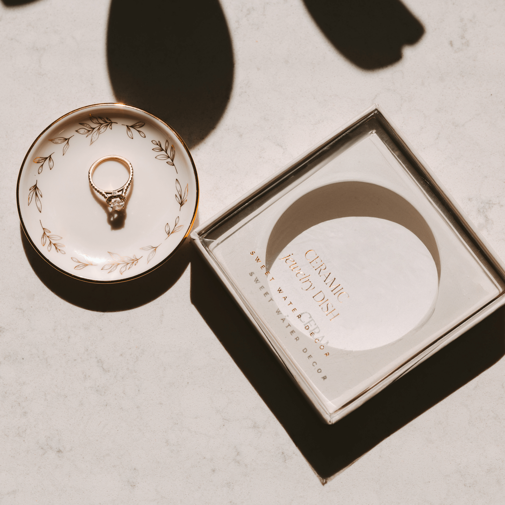 Gold ring on a decorative ceramic dish with a matching box on a light background