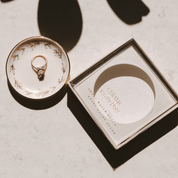 Gold ring on a decorative ceramic dish with a matching box on a light background