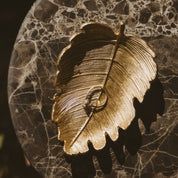 Gold leaf-shaped ring holder with a ring on a marble surface