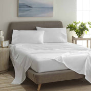 White bedding set on a bed in a bedroom with a painting and plant in the background.