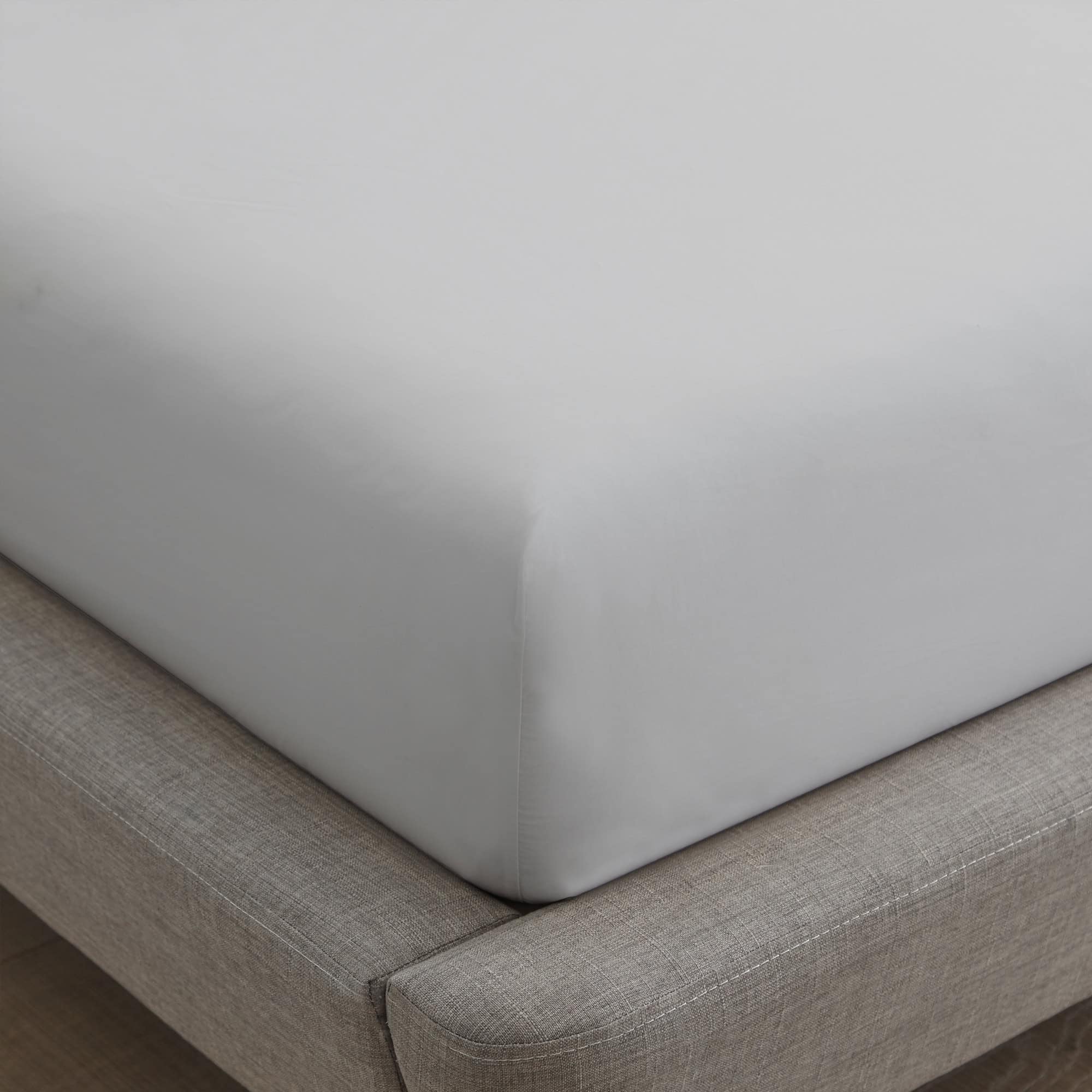 Gray fitted sheet on a bed with a wooden floor.