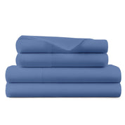 A stack of four folded blue bedding sheets, including a flat sheet, fitted sheet, pillowcases, and a pillowcase, on a solid white background.