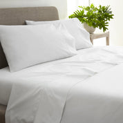 White bed sheets and pillows on a bed with a plant in the background
