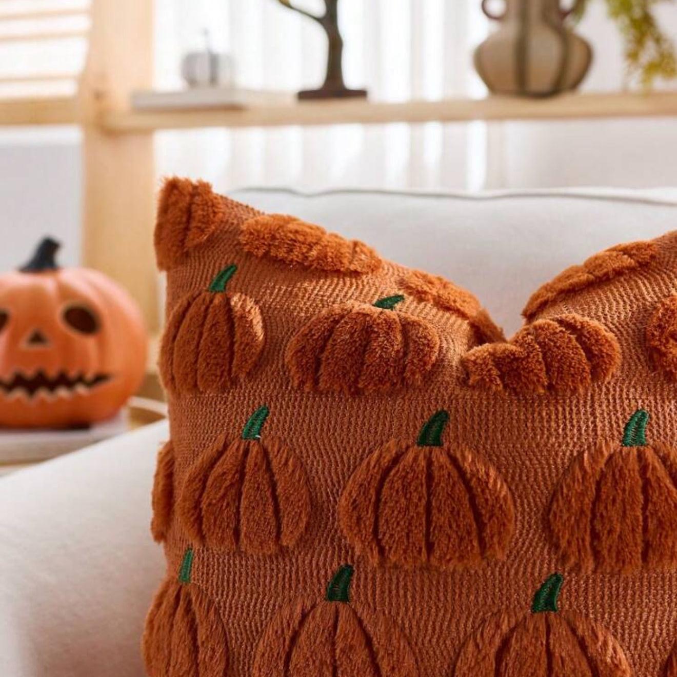 Decorative pillow with pumpkin pattern on a couch with a pumpkin decoration in the background.