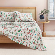 Christmas-themed bedspread with reindeer, Santa, and trees on a bed in a bedroom.