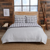 Bed with checkered bedding in a rustic bedroom setting with wooden walls and a window.