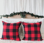 Red and black checkered pillows on a bed with a decorative headboard and garland.