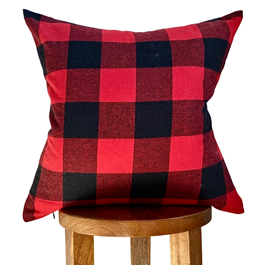 Red and black checkered pillow on a wooden stool against a white background