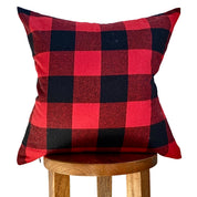 Red and black checkered pillow on a wooden stool against a white background