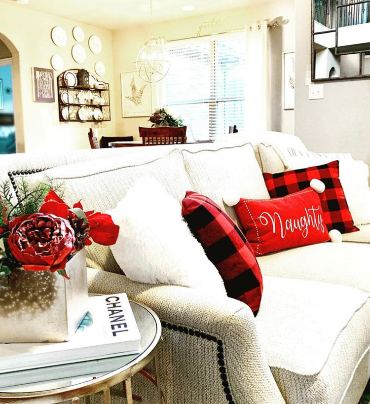 Living room with a white sofa decorated with red and black pillows, a Christmas wreath, and a Chanel book.