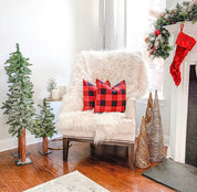 Cozy living room with a chair draped with a white fur throw and plaid pillows, surrounded by Christmas decorations.