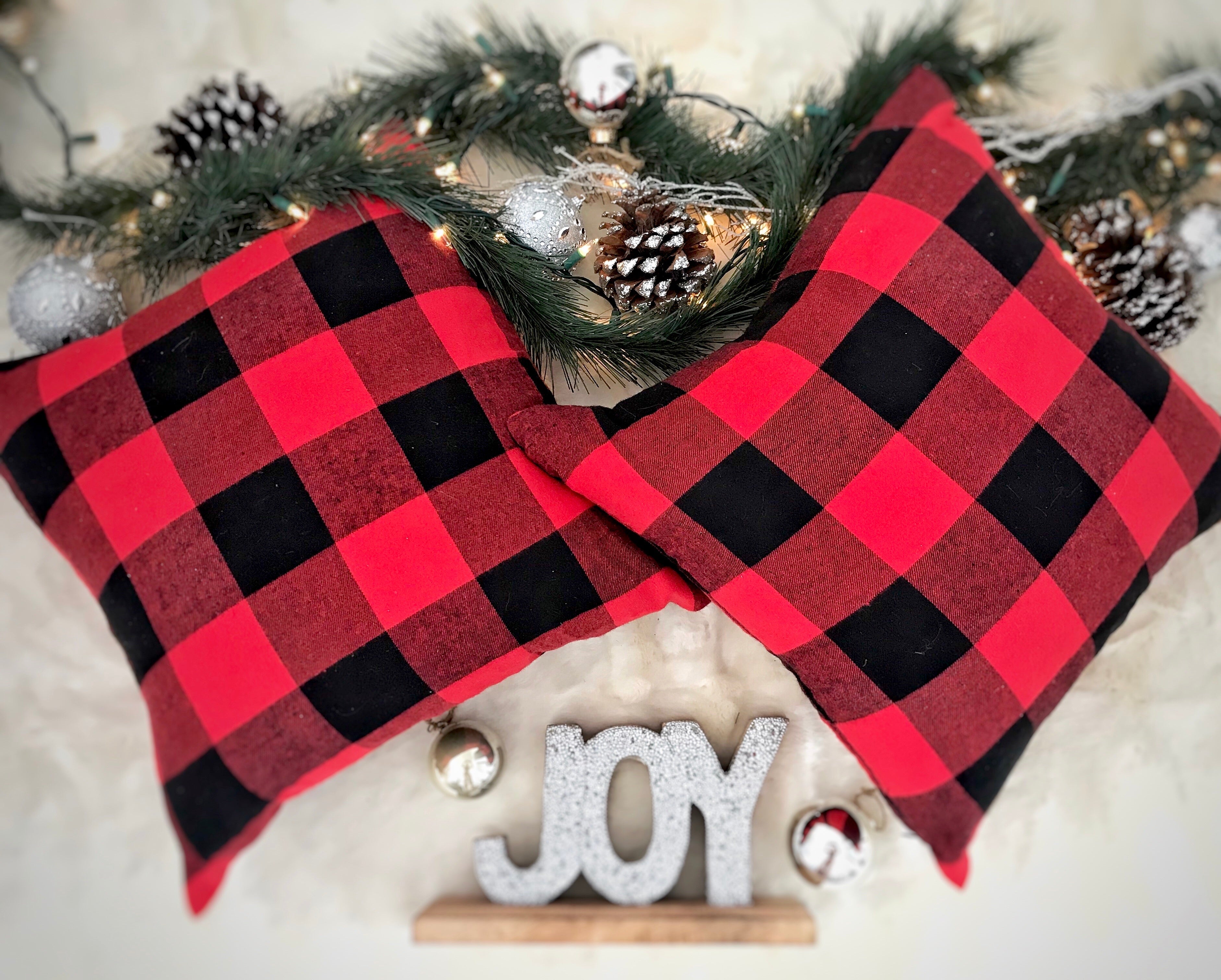 Red and black checkered pillow with Christmas decorations including pine cones and 'JOY' sign.