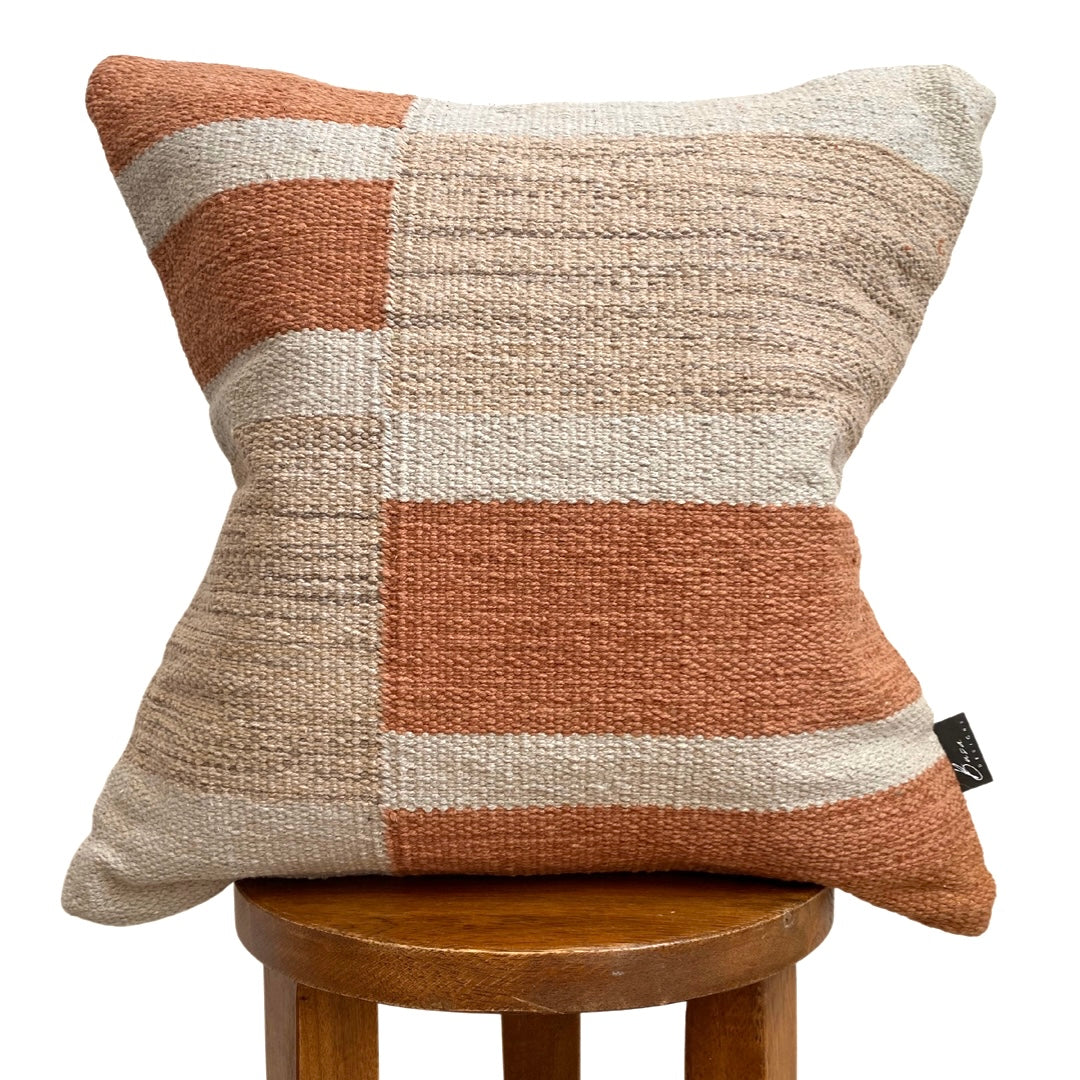 Decorative pillow with brown and beige checkered pattern on a wooden stool against a white background