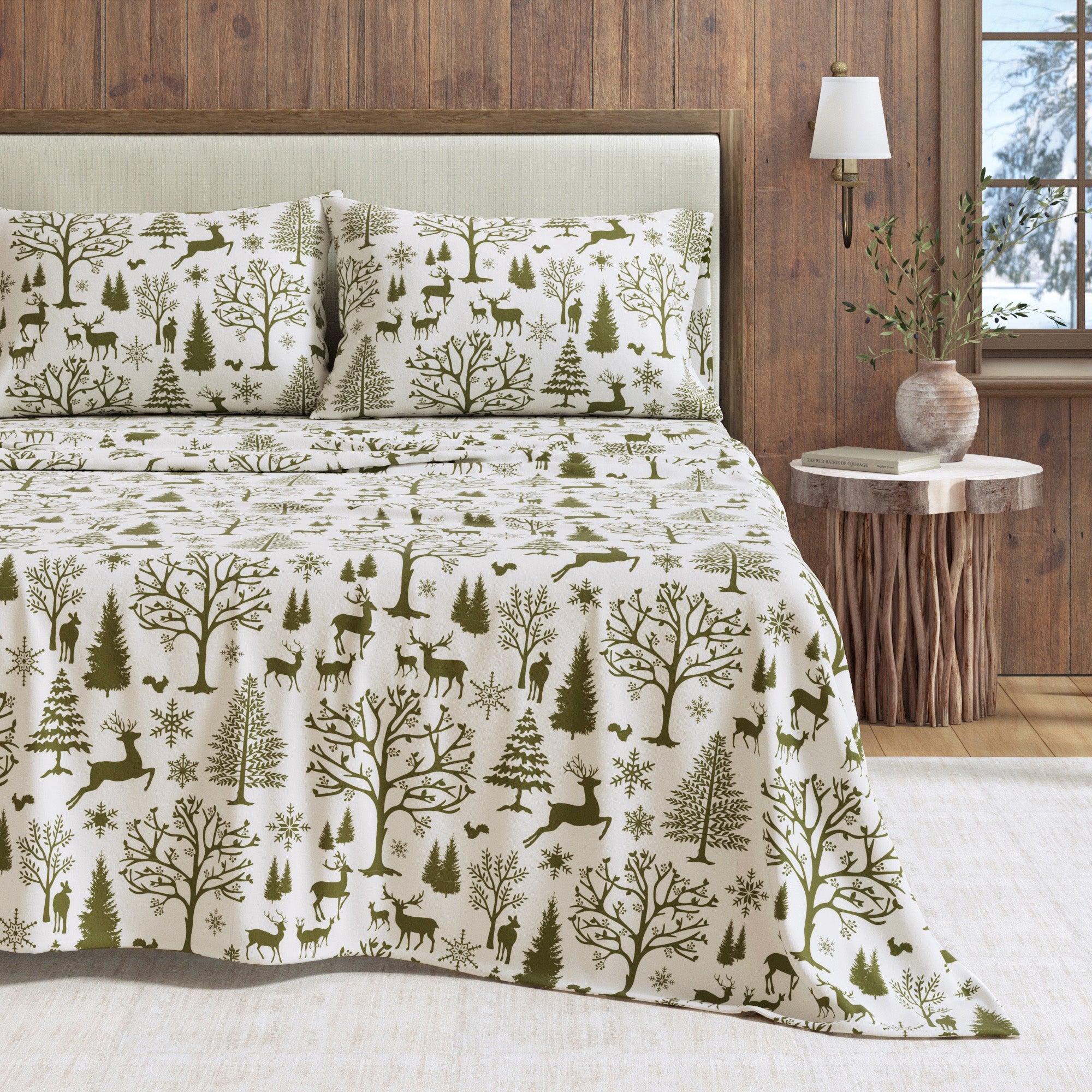 Bedding set with forest pattern on a bed in a room with wooden walls and a lamp.