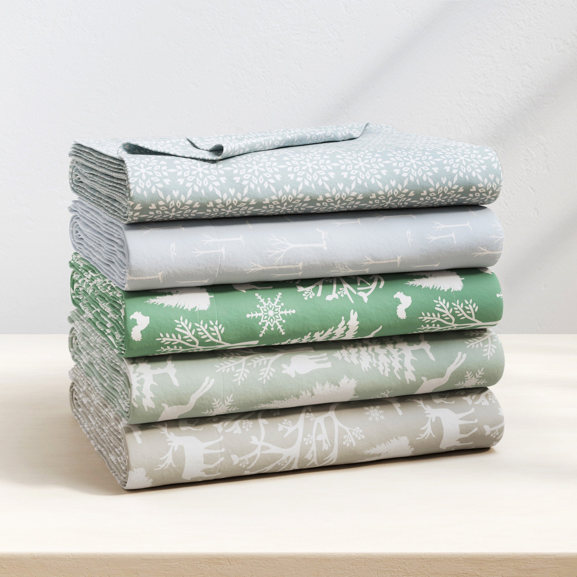 Stack of folded fabric sheets with nature-themed patterns on a white surface.