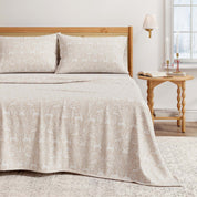 Beige bedspread on a bed with a wooden headboard and side table in a bedroom setting.