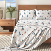 Bed with patterned bedding featuring deer and trees, next to a wooden nightstand with a plant.