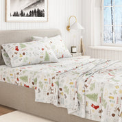 Christmas-themed bedspread on a bed in a bedroom with a window and lamp in the background.