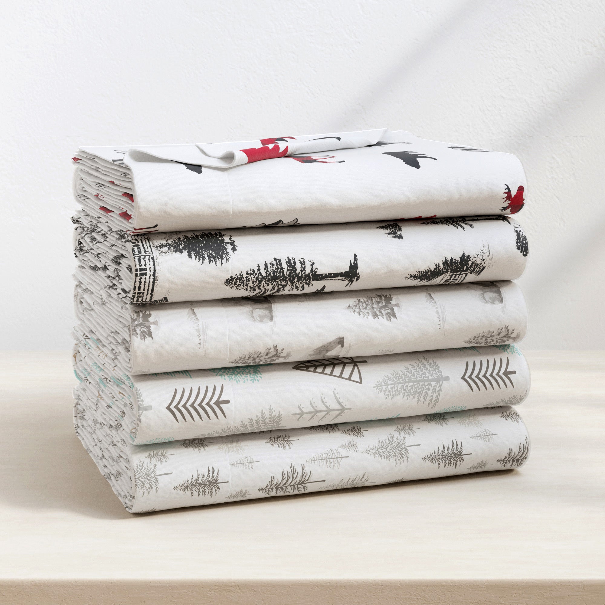 Stack of folded bed sheets with nature-themed design on a light background
